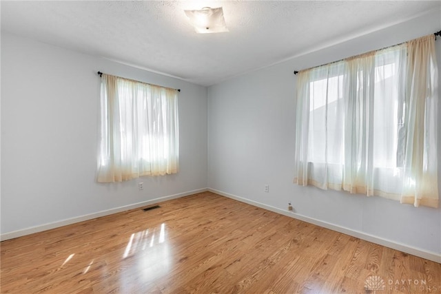 spare room with visible vents, a textured ceiling, baseboards, and wood finished floors