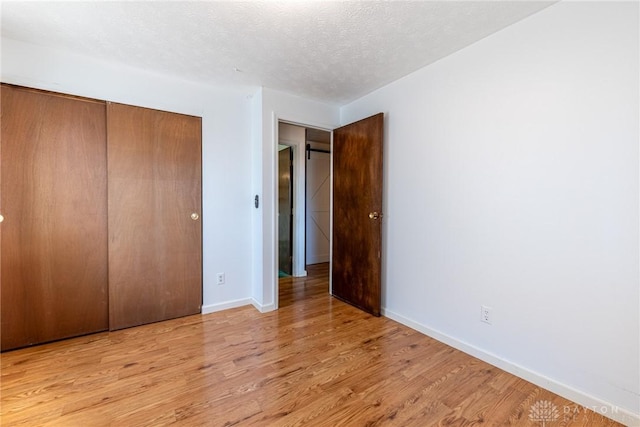 unfurnished bedroom with a closet, baseboards, a textured ceiling, and wood finished floors