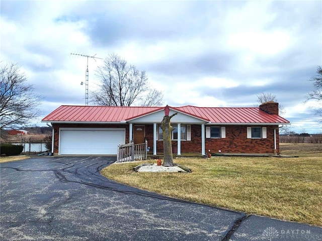 ranch-style home featuring brick siding, a front lawn, aphalt driveway, a chimney, and an attached garage