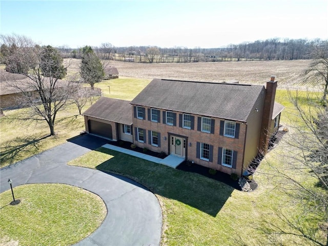 view of front of property featuring a front yard, a chimney, a rural view, a garage, and aphalt driveway