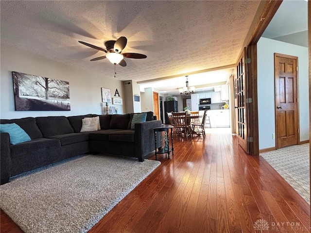 living room featuring ceiling fan with notable chandelier, a textured ceiling, dark wood-type flooring, and baseboards