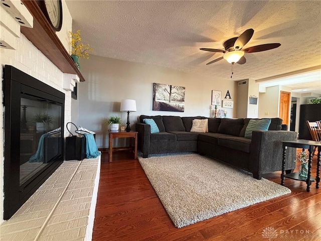 living room with a ceiling fan, wood finished floors, a fireplace, and a textured ceiling