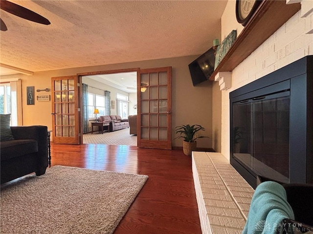 living room featuring a textured ceiling, a brick fireplace, wood finished floors, and a ceiling fan