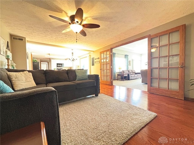 living area featuring visible vents, ceiling fan with notable chandelier, a textured ceiling, and wood finished floors