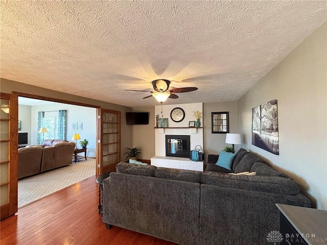 living room with a textured ceiling, a fireplace, wood-type flooring, and ceiling fan