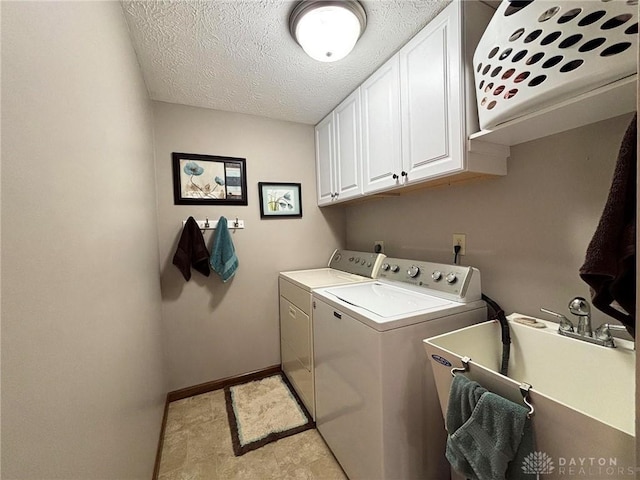 washroom with baseboards, cabinet space, a sink, a textured ceiling, and washer and dryer