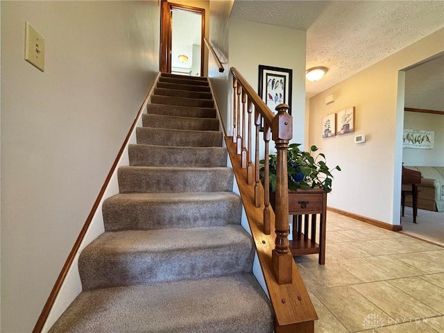 staircase featuring a textured ceiling and baseboards