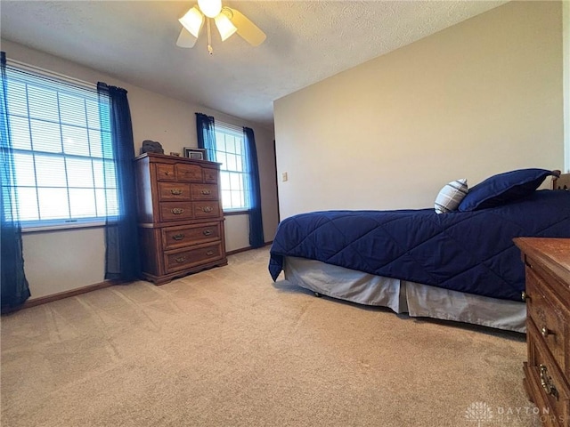 bedroom featuring a ceiling fan, light colored carpet, baseboards, and a textured ceiling