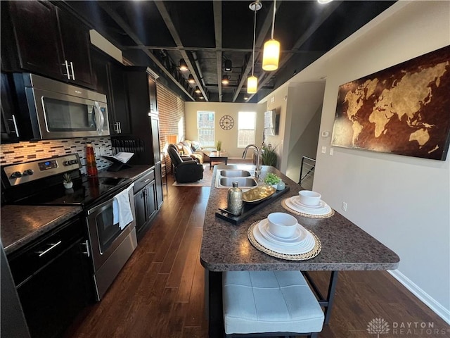 kitchen featuring dark wood finished floors, open floor plan, appliances with stainless steel finishes, dark cabinetry, and a sink