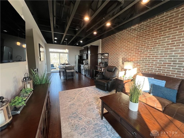 living room featuring brick wall and dark wood-style flooring