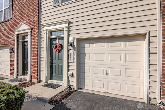 view of exterior entry featuring brick siding, driveway, and a garage