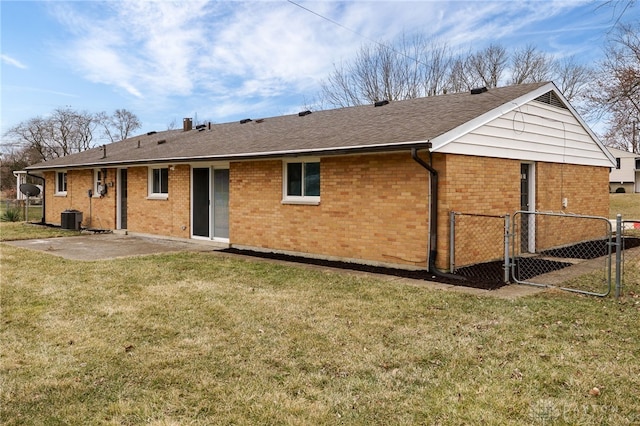 rear view of house with a gate, fence, central AC unit, a yard, and brick siding