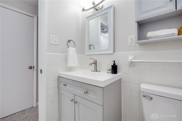 half bathroom with a wainscoted wall, toilet, tile walls, and vanity