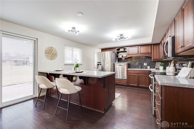 kitchen featuring a breakfast bar area, open shelves, dark wood-style flooring, stainless steel appliances, and decorative backsplash