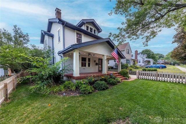 view of front of home featuring a front lawn, a porch, fence, and a chimney