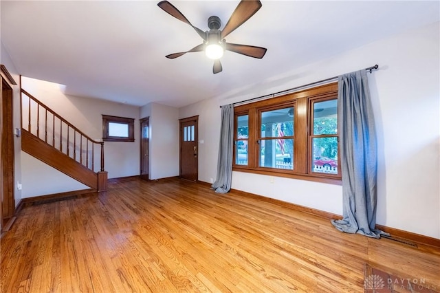 unfurnished living room with light wood-type flooring, baseboards, ceiling fan, and stairs