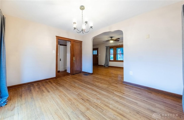 unfurnished room with ceiling fan with notable chandelier, light wood-style floors, arched walkways, and baseboards