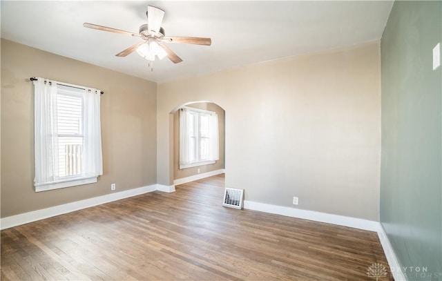 spare room featuring wood finished floors, baseboards, arched walkways, and ceiling fan