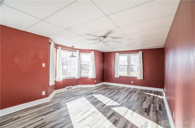 empty room with visible vents, a paneled ceiling, a healthy amount of sunlight, and wood finished floors