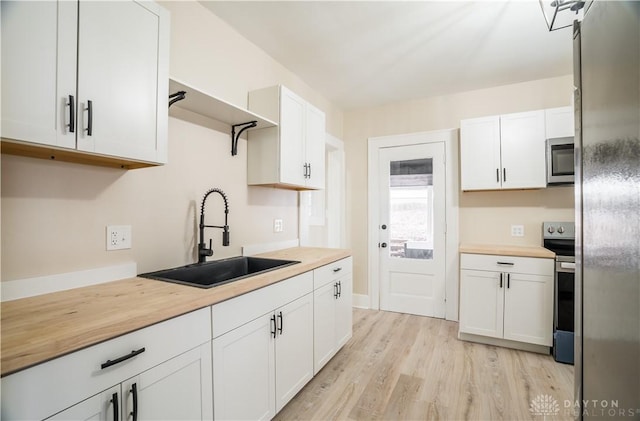 kitchen featuring light wood-style flooring, a sink, wood counters, white cabinetry, and appliances with stainless steel finishes