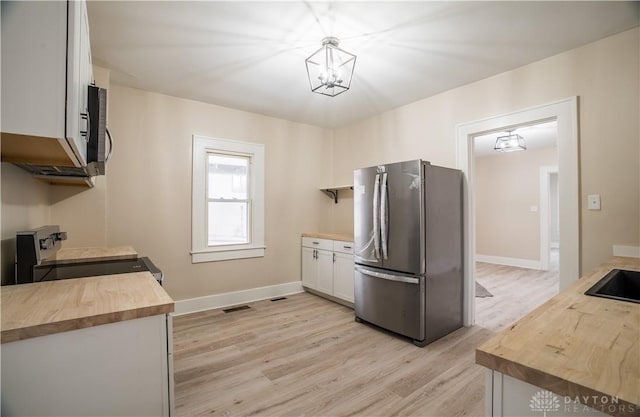 kitchen with baseboards, light wood-type flooring, appliances with stainless steel finishes, and butcher block counters