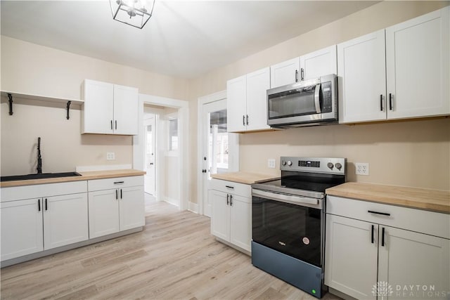 kitchen featuring wooden counters, appliances with stainless steel finishes, light wood-style floors, white cabinets, and a sink