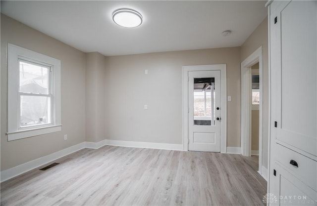 empty room featuring light wood finished floors, visible vents, and baseboards