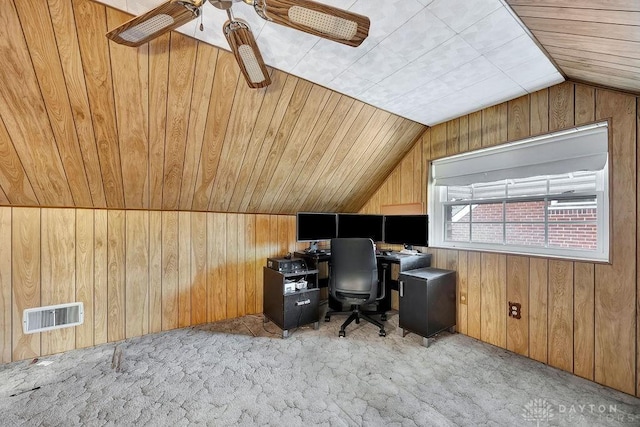 office featuring wooden walls, a ceiling fan, visible vents, vaulted ceiling, and light colored carpet