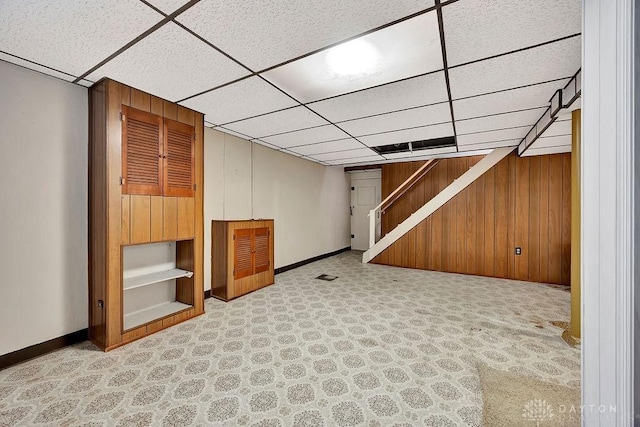 finished basement featuring wooden walls, carpet, baseboards, a drop ceiling, and stairs