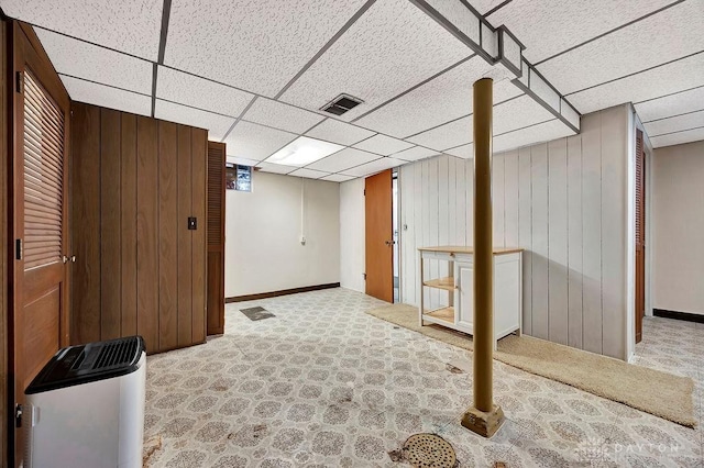 finished below grade area featuring baseboards, visible vents, a drop ceiling, wood walls, and carpet flooring