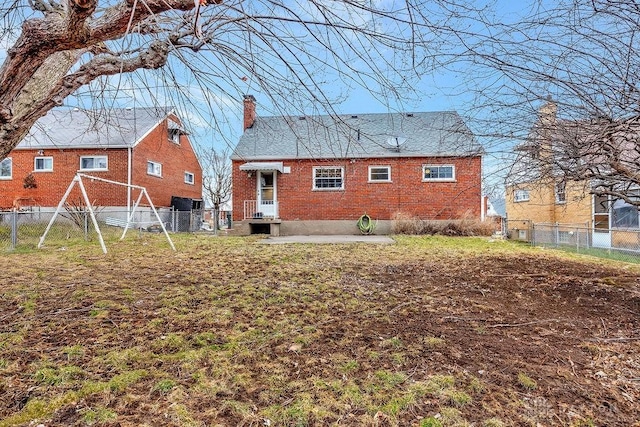 rear view of property featuring brick siding, a lawn, a chimney, and fence