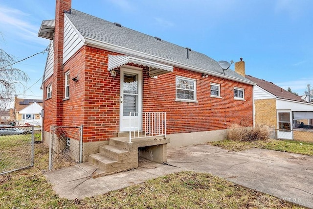 back of house with a shingled roof, fence, brick siding, and a chimney