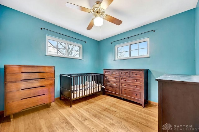 bedroom featuring a nursery area, a ceiling fan, baseboards, and light wood finished floors