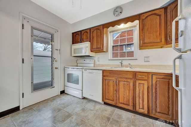 kitchen with brown cabinetry, white appliances, light countertops, and a sink