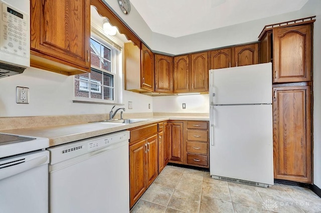 kitchen featuring white appliances, light countertops, brown cabinets, and a sink