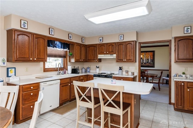 kitchen with a breakfast bar, a sink, under cabinet range hood, white appliances, and light countertops