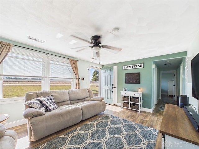 living area featuring visible vents, baseboards, a healthy amount of sunlight, and wood finished floors