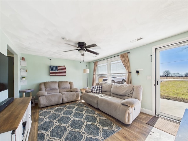 living area with baseboards, wood finished floors, visible vents, and ceiling fan