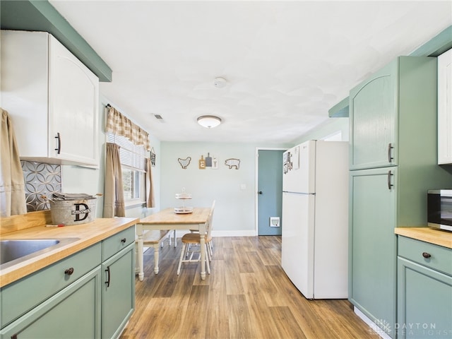 kitchen with backsplash, freestanding refrigerator, green cabinets, butcher block counters, and light wood finished floors