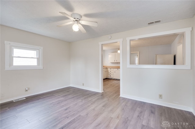 empty room featuring visible vents, a textured ceiling, a ceiling fan, and wood finished floors