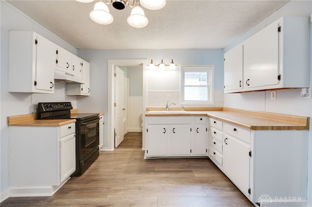 kitchen with electric range, under cabinet range hood, a sink, a textured ceiling, and light wood-style floors