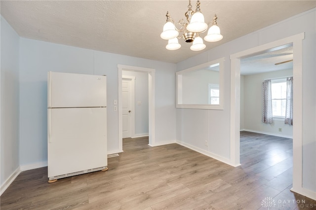 unfurnished dining area with a chandelier, a textured ceiling, baseboards, and wood finished floors