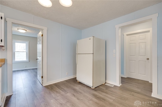 kitchen with light wood-style flooring, baseboards, freestanding refrigerator, and a textured ceiling