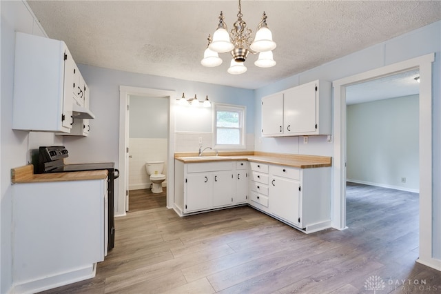 kitchen with range with electric cooktop, light wood-style flooring, a sink, a textured ceiling, and white cabinetry