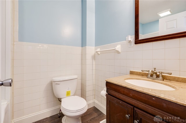 bathroom featuring a wainscoted wall, toilet, wood finished floors, tile walls, and vanity