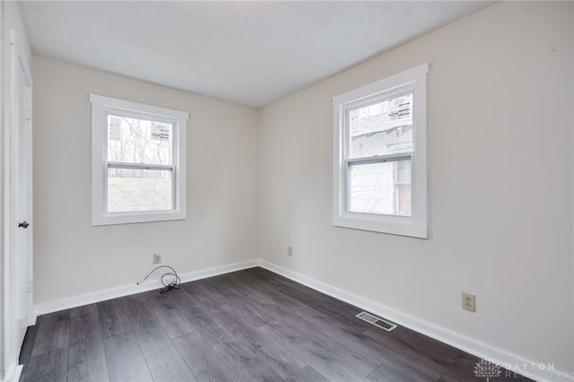 unfurnished room featuring visible vents, baseboards, and dark wood-style flooring