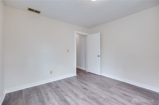 unfurnished room with visible vents, light wood-style flooring, a textured ceiling, and baseboards