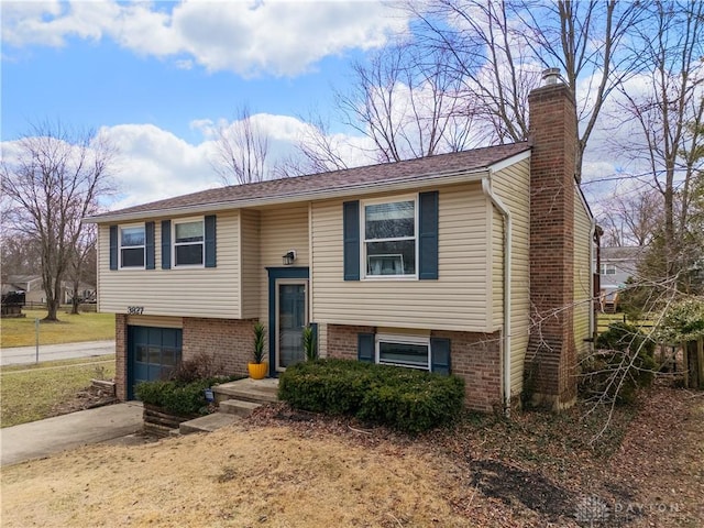 bi-level home with concrete driveway, brick siding, a garage, and a chimney