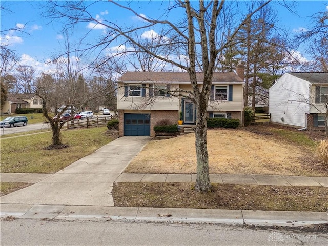 raised ranch featuring brick siding, concrete driveway, a front yard, a chimney, and an attached garage