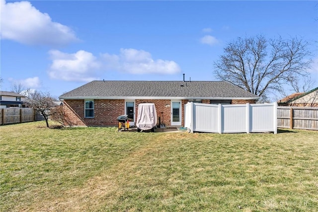 back of house with a yard, a fenced backyard, brick siding, and roof with shingles